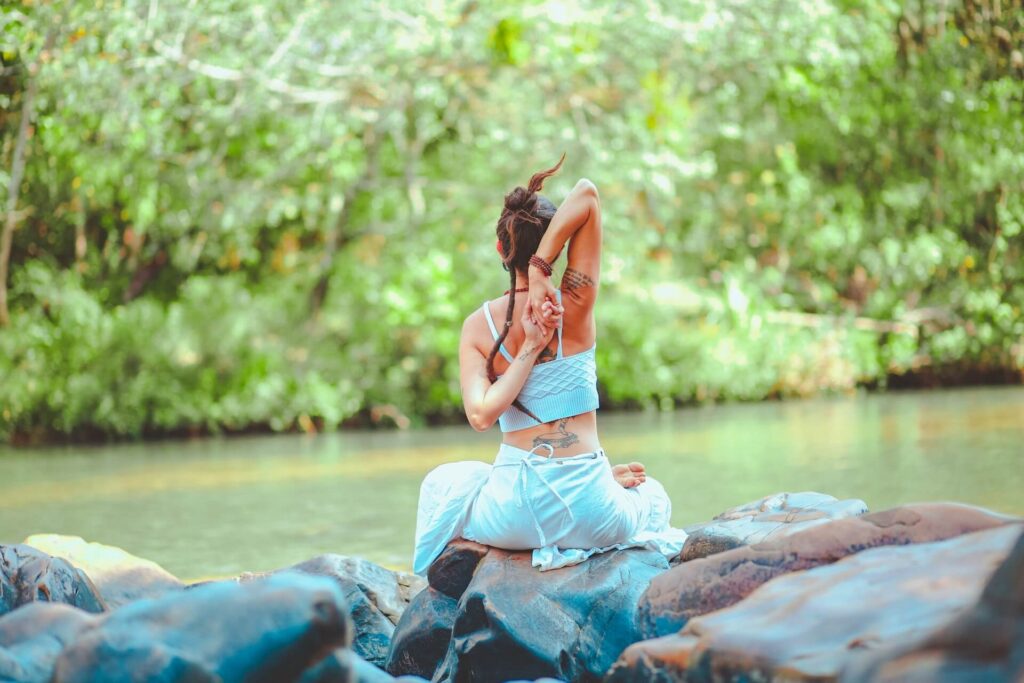 Frau, die am Fluss sitzt und Yoga macht